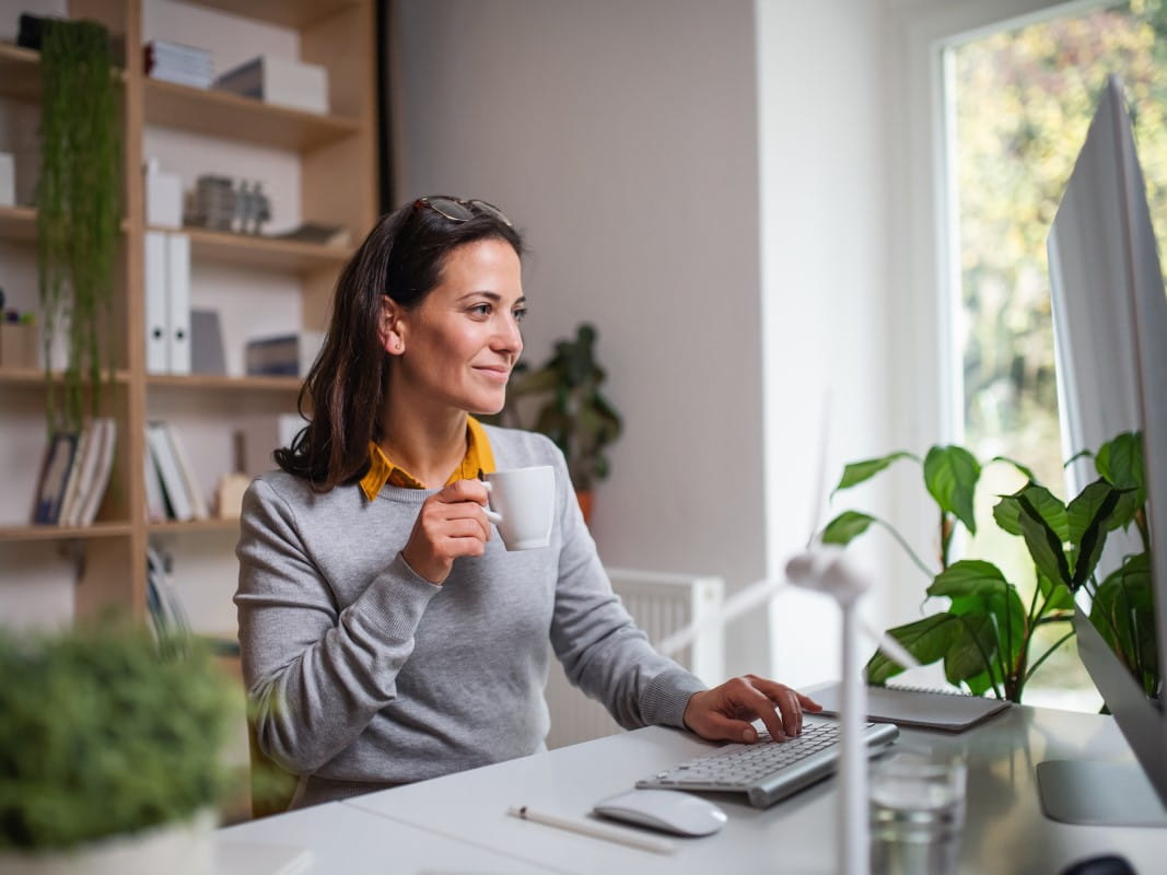 Woman drinking cup of tea whilst using computer
