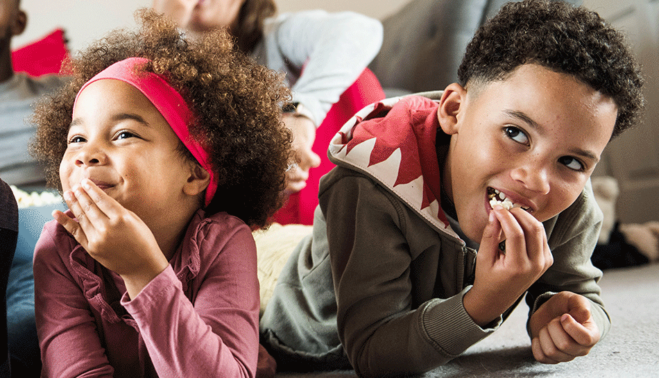 Children lying on carpet eating popcorn